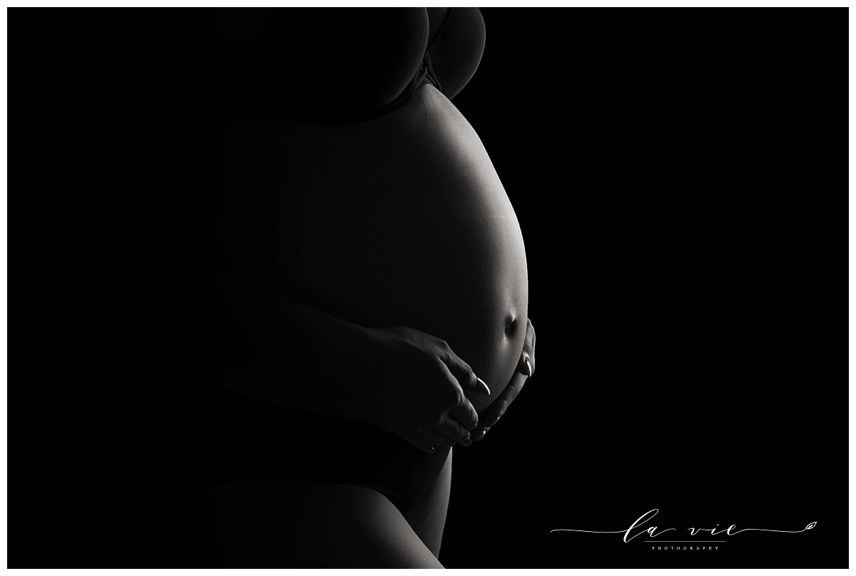Black and white closeup of pregnant belly with dramatic studio lighting