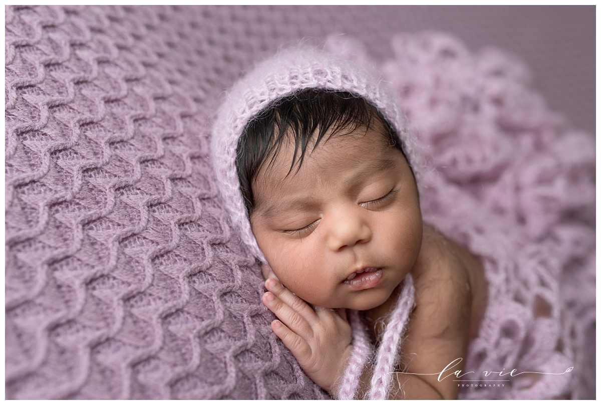 Close up of newborn baby's face and hands on purple blanket