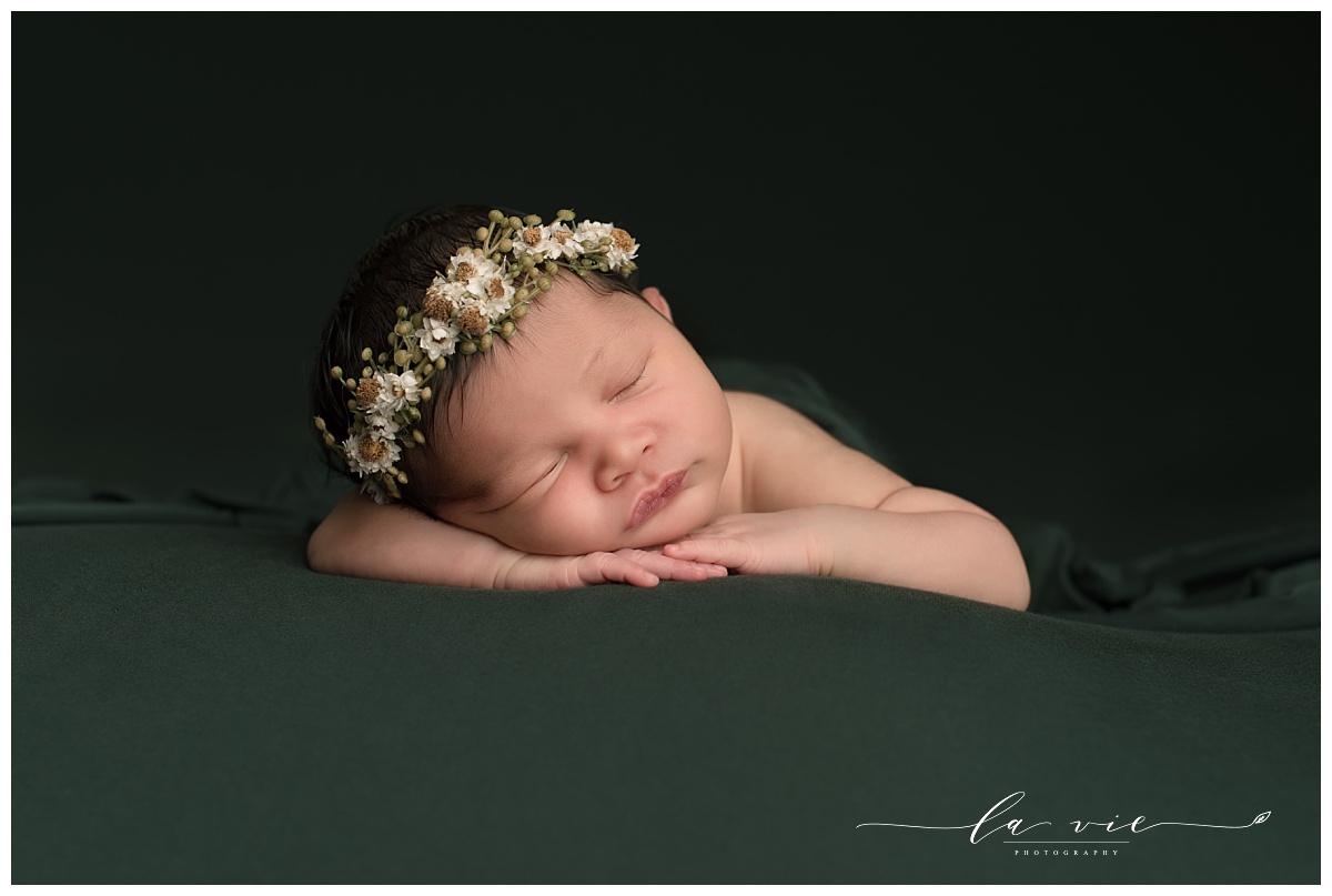 newborn girl with floral headband on dark green background
